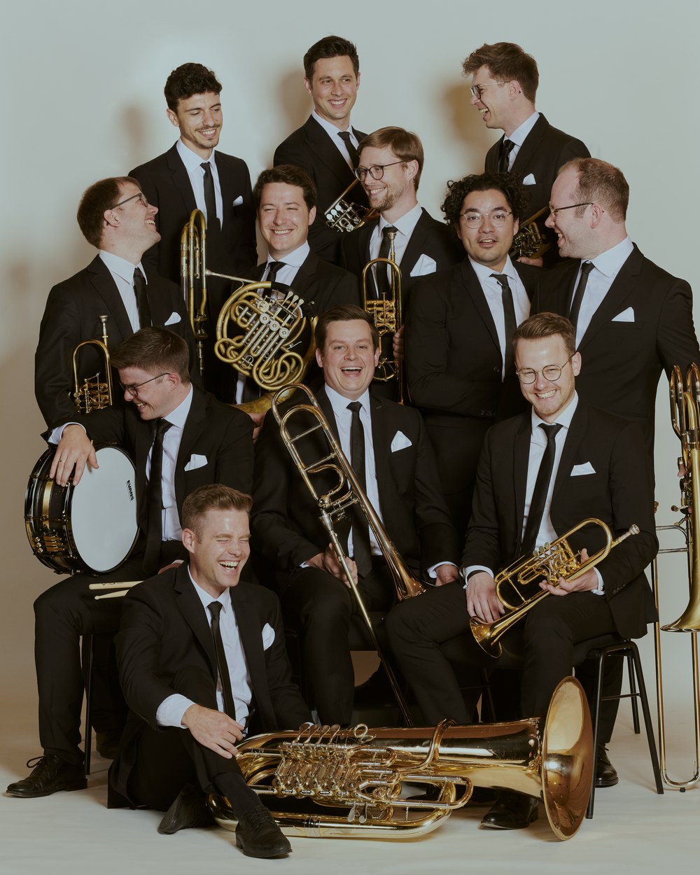 Gruppenfoto von Salaputia Brass: elf Musiker im schwarzen Anzug mit ihren Blechblasinstrumenten und einer Kleinen Trommel.
